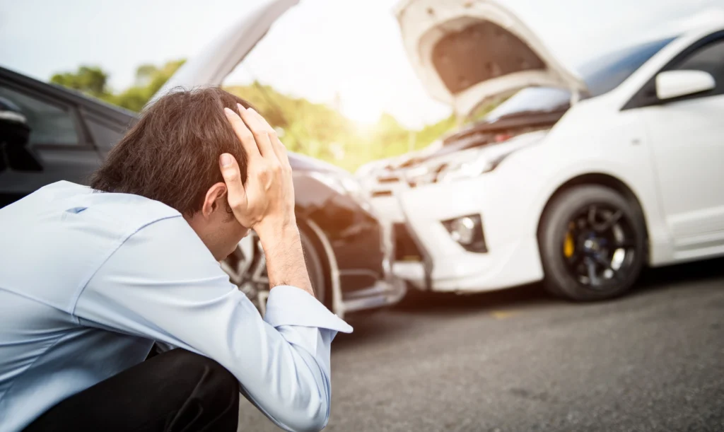 man in front of car crash holding his head